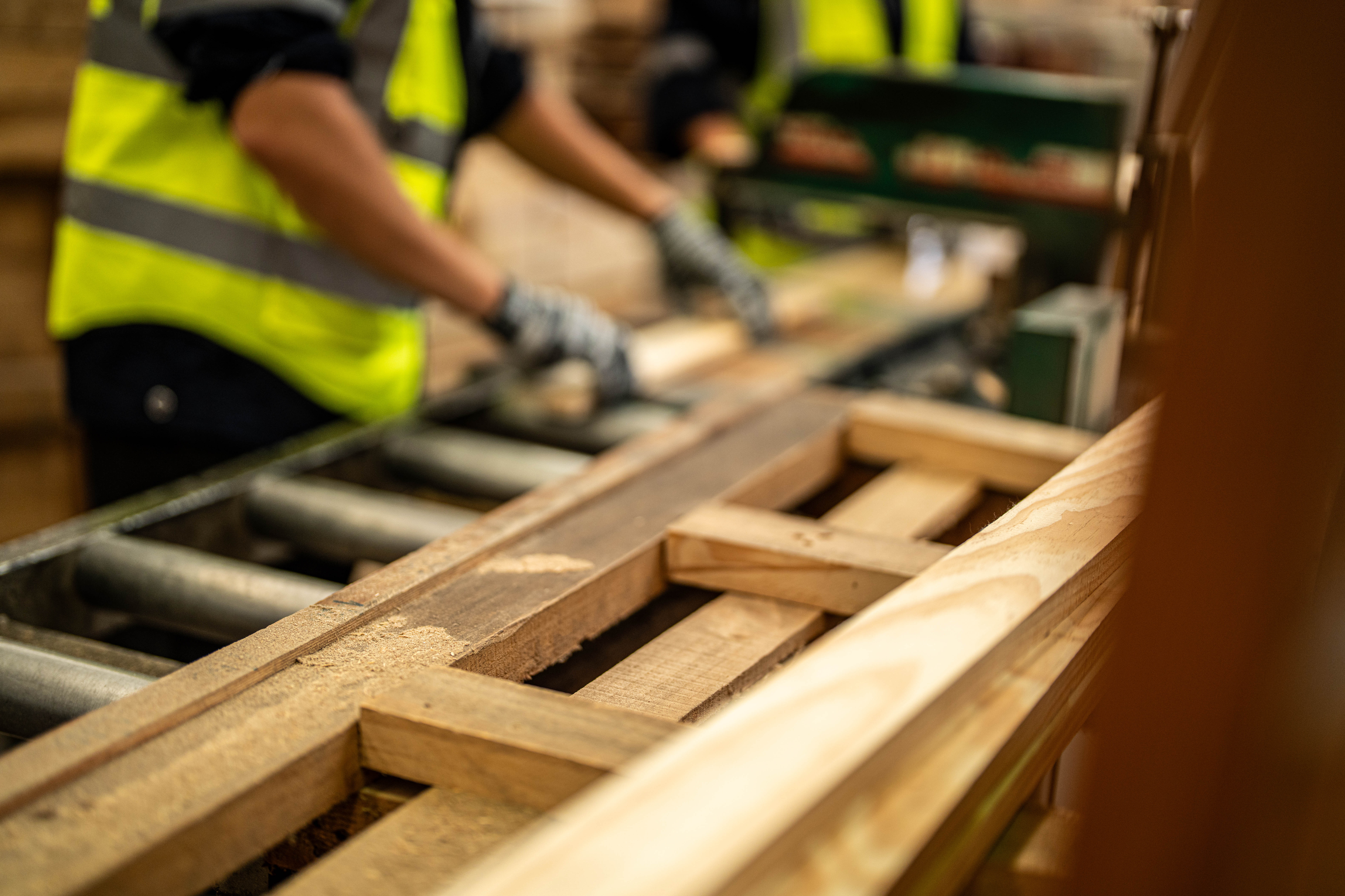 hands man cleaning timber wood in dark warehouse industry. Team worker carpenter wearing safety uniform and hard hat working and checking the quality of wooden products at workshop.