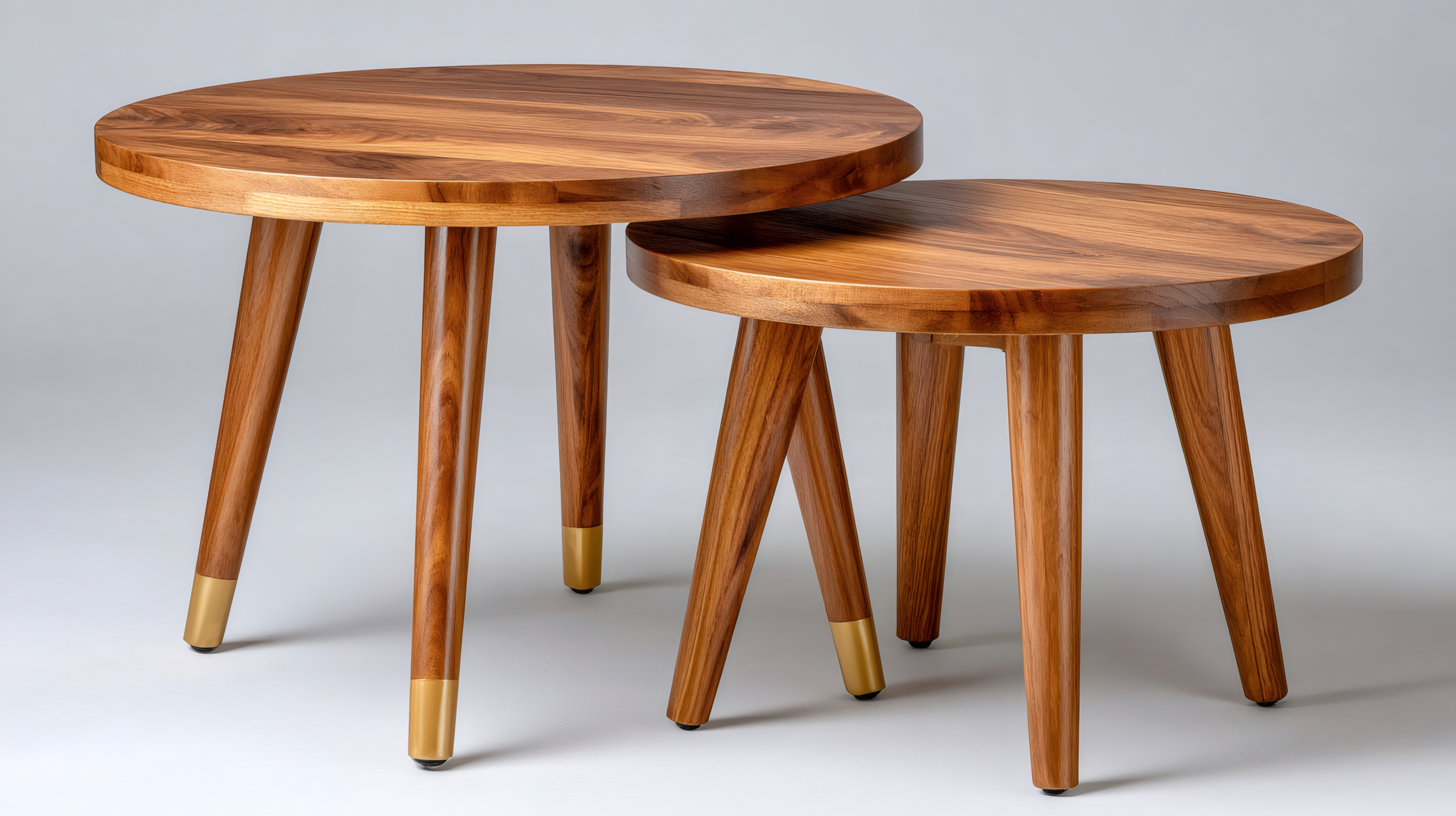 Nesting circular wooden side tables with gold accents Nesting circular wooden side tables with tripod legs and gold caps on a neutral background